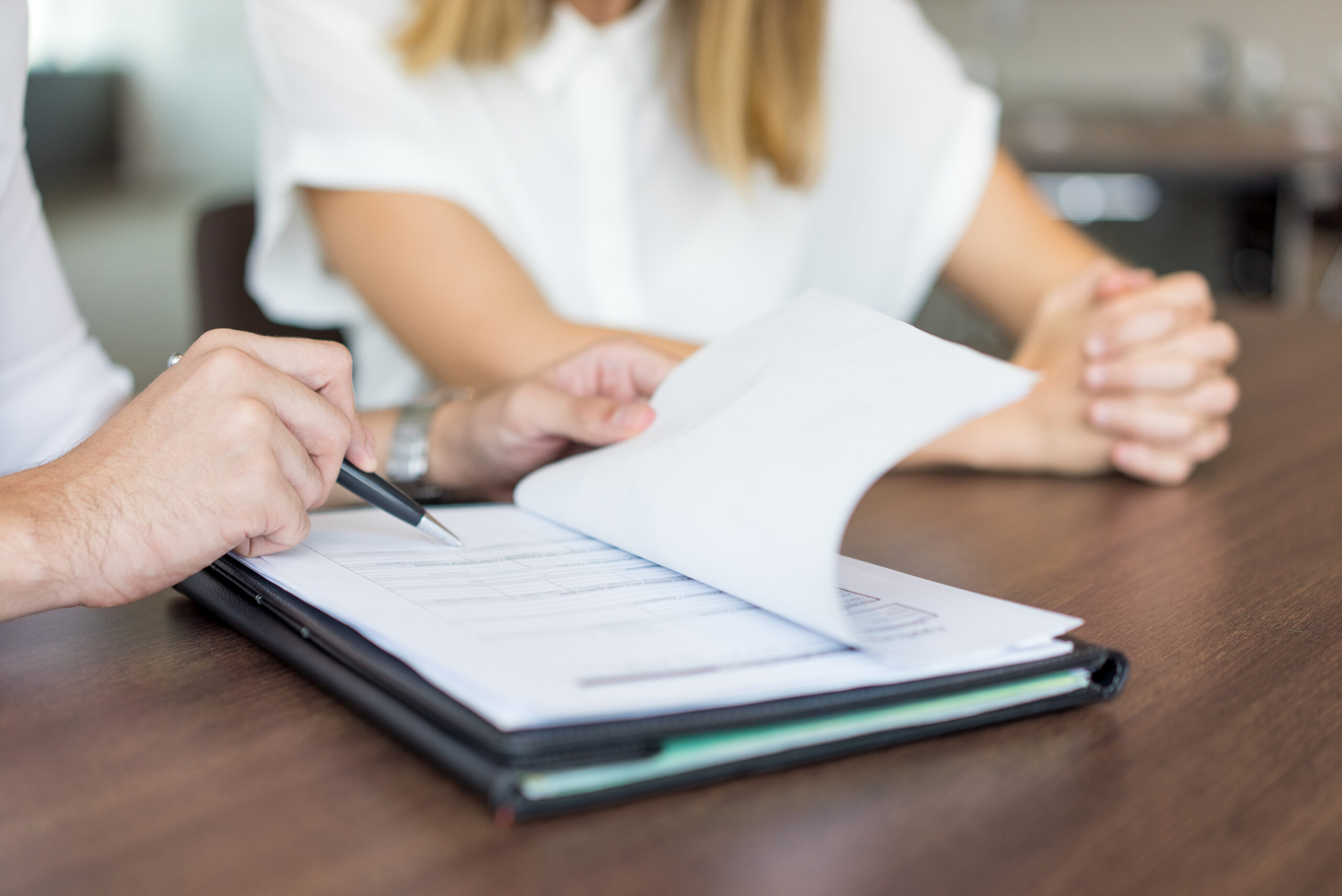 Hands of male executive showing contract to female partner at meeting. Close-up of young Caucasian business colleagues sitting at table and discussing document. Teamwork and partnership concept
